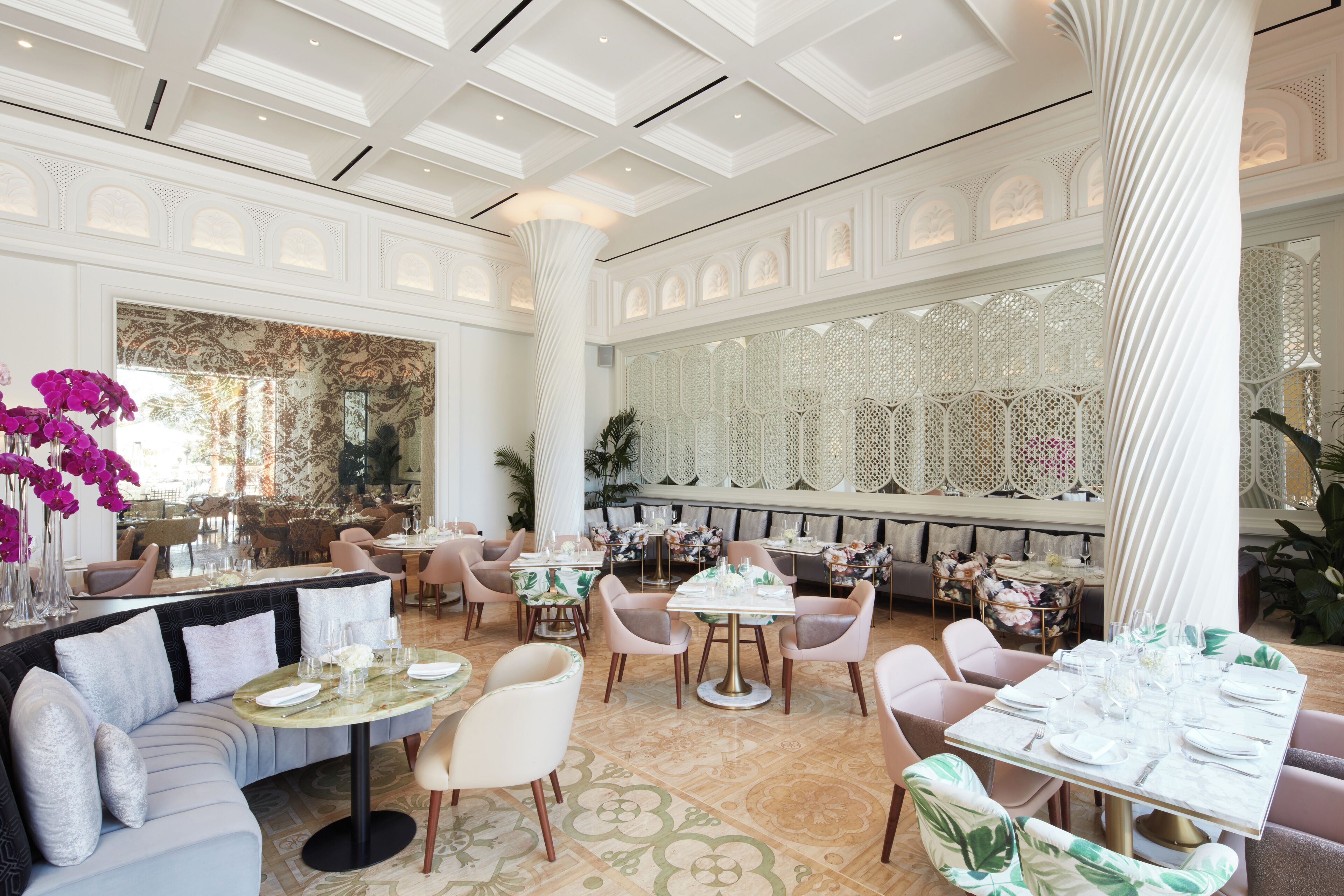 Un vaste espace dédié à la salle à manger, avec plusieurs tables et chaises, un grand miroir décoratif et un sol à motifs.