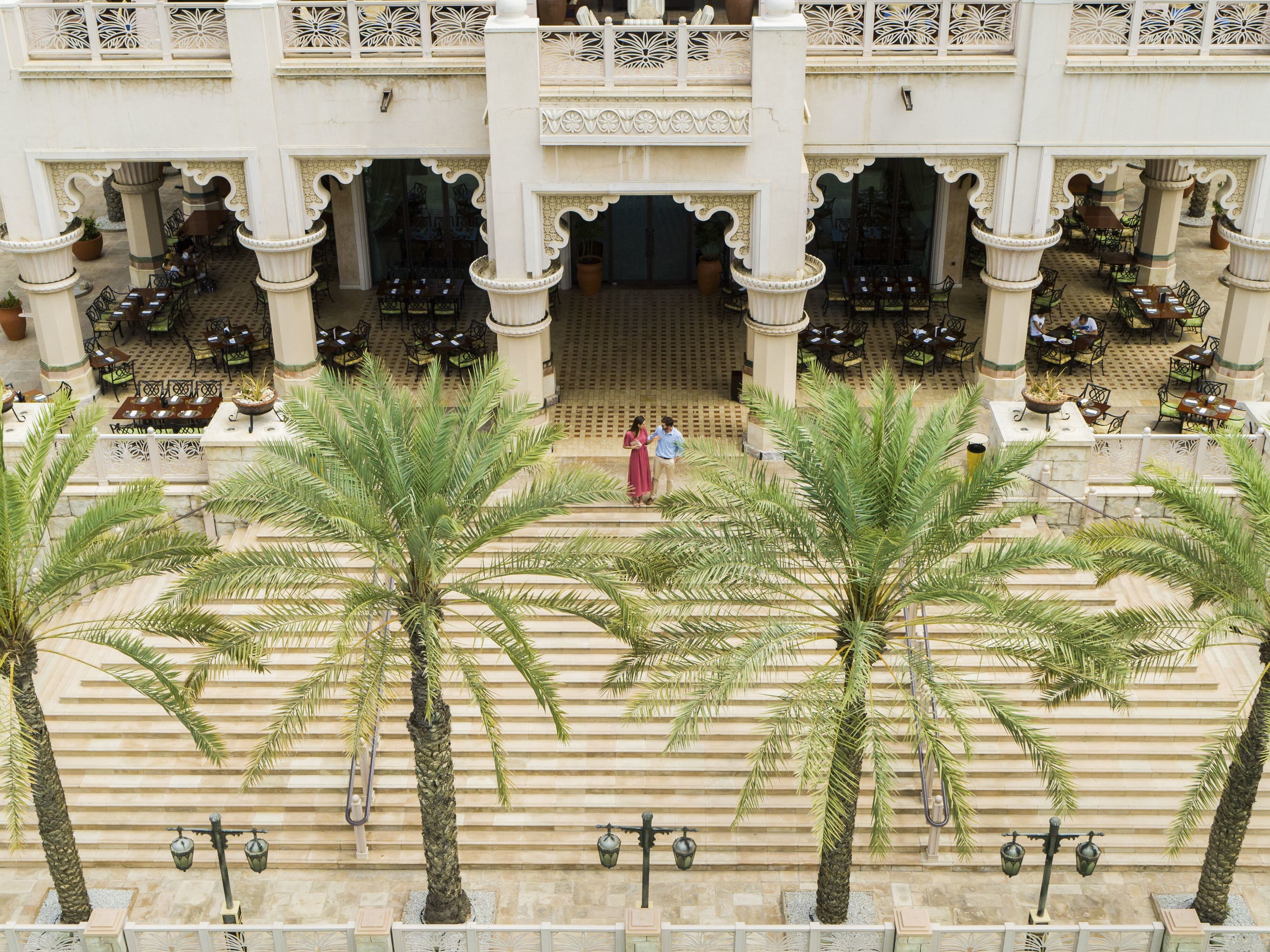 A courtyard with palm trees, outdoor seating, and a central entrance.