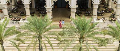 A courtyard with palm trees, outdoor seating, and a central entrance.