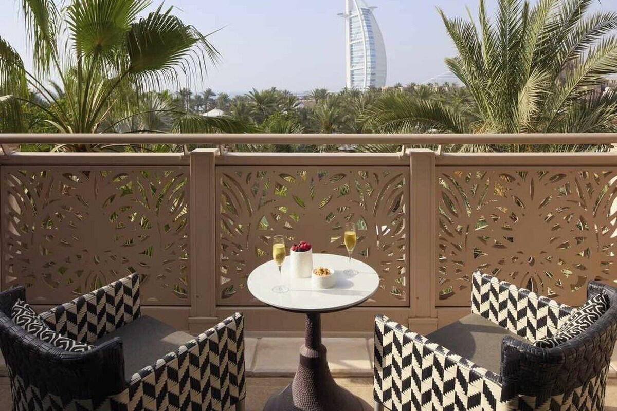 An outdoor seating area with a view of a distinctive sail-shaped building, surrounded by palm trees.