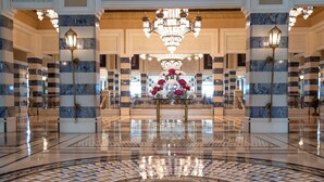 A grand lobby with a marble floor, a central chandelier, and a decorative fountain.