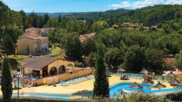 A resort with a swimming pool, sun loungers, and a view of the surrounding forest.