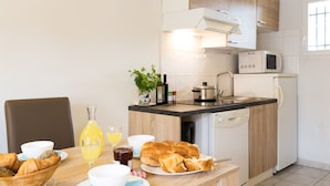 A kitchen with a dining table set for breakfast, including croissants, bread, and a bottle of orange juice. - Résidence Odalys Domaine des Hauts de Salavas (Salavas)