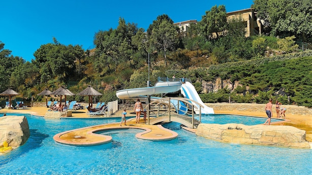 A pool area with a water slide, lounge chairs, and a rocky landscape in the background. - Résidence Odalys Domaine des Hauts de Salavas (Salavas)