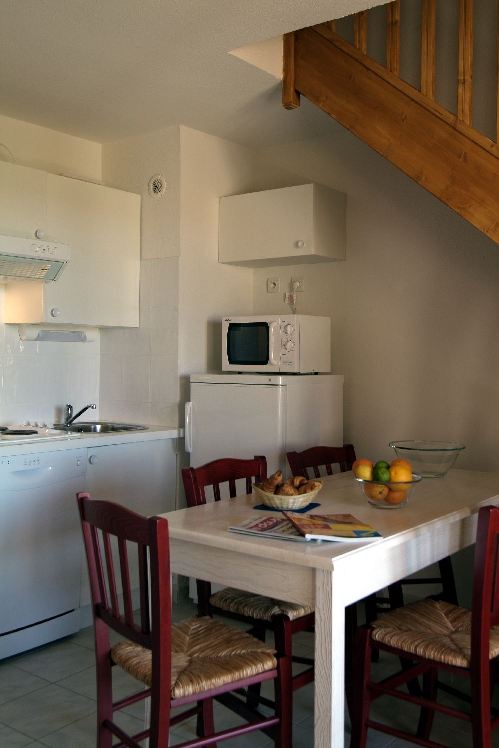 Una cocina compacta con microondas, refrigerador y una mesa de comedor con sillas.