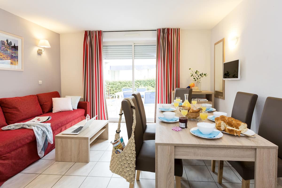 Ein modernes Wohnzimmer mit einem roten Sofa, einem Holztisch und einem Essbereich, der für ein Frühstück gedeckt ist.