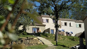 A building with a stone staircase leading to a door, surrounded by greenery and trees. - Résidence Odalys Domaine des Hauts de Salavas (Salavas)