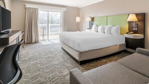 A hotel room with a large bed, a desk with a flat-screen TV, a chair, and a sofa.