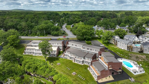 An aerial view of a residential area with a large building complex, a swimming pool, and a road.