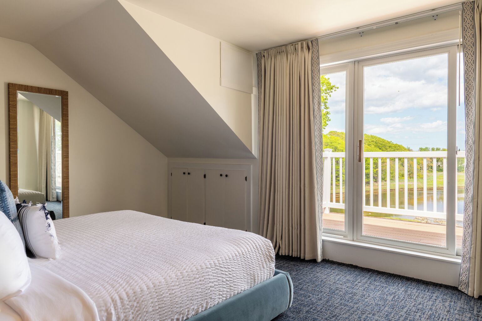 Een slaapkamer met een groot bed, een spiegel, een kledingkast en een balkon met uitzicht op groen.