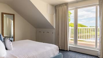 Een slaapkamer met een groot bed, een spiegel, een kledingkast en een balkon met uitzicht op groen.
