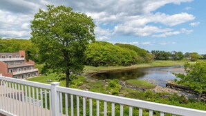 A balcony with a view of a river, lush greenery, and a building with a brick facade. - Ogunquit River Inn & Suites (Ogunquit)
