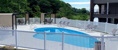 A swimming pool with a white fence, lounge chairs, and a covered seating area.