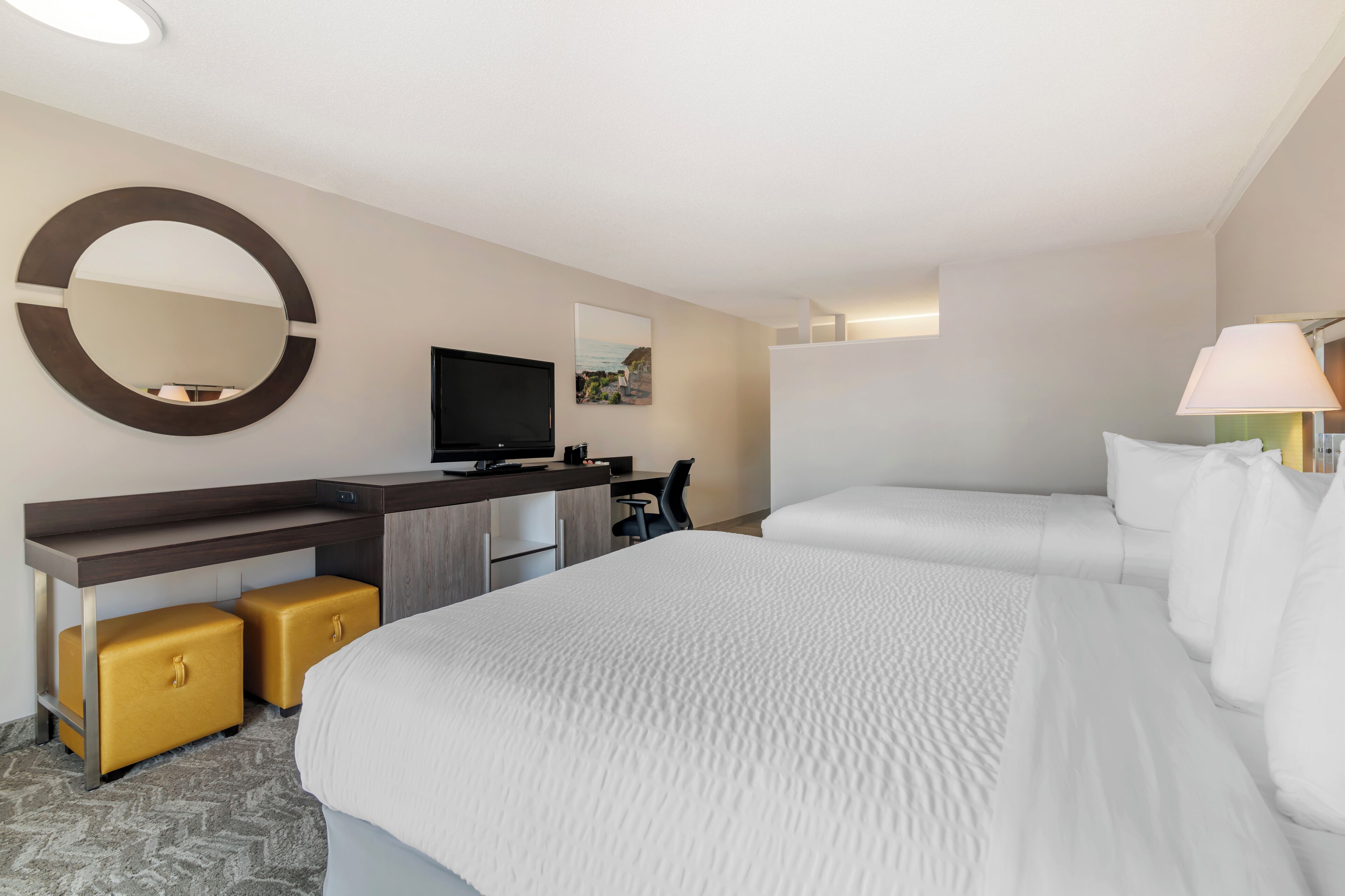 A hotel room with a large bed, a desk with a flat-screen TV, a mirror, and a lamp.