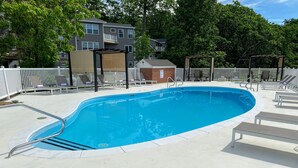 A rectangular swimming pool with a metal ladder, surrounded by a white fence and lounge chairs.