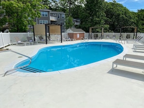 A rectangular swimming pool with a metal ladder, surrounded by a white fence and lounge chairs.