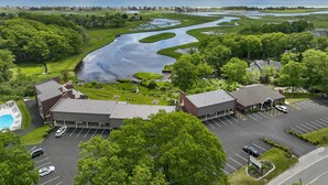 An aerial view of a hotel with a swimming pool, parking lot, and a large body of water with a winding path. - Ogunquit River Inn & Suites (Ogunquit)