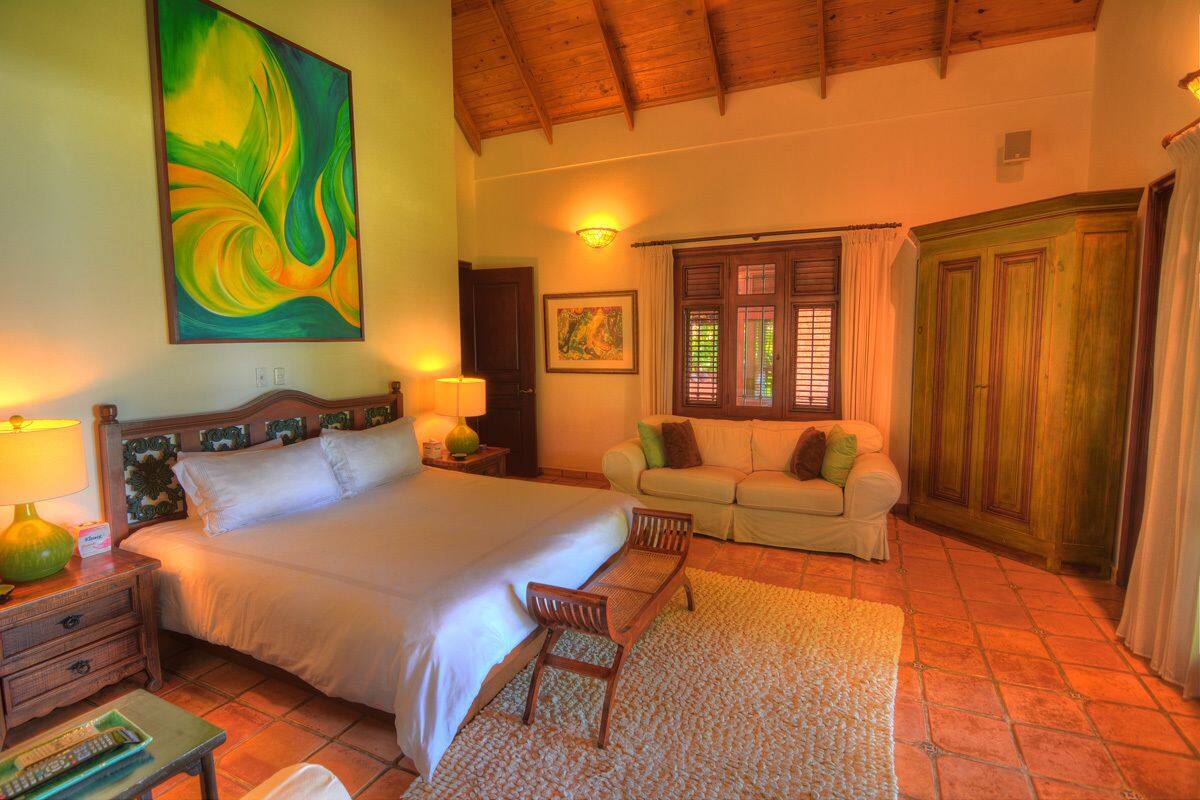 A spacious bedroom with a large bed, a sitting area with a sofa, and a wooden wardrobe.