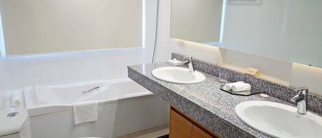 A modern bathroom with a double sink, a large mirror, a bathtub, and a toilet.