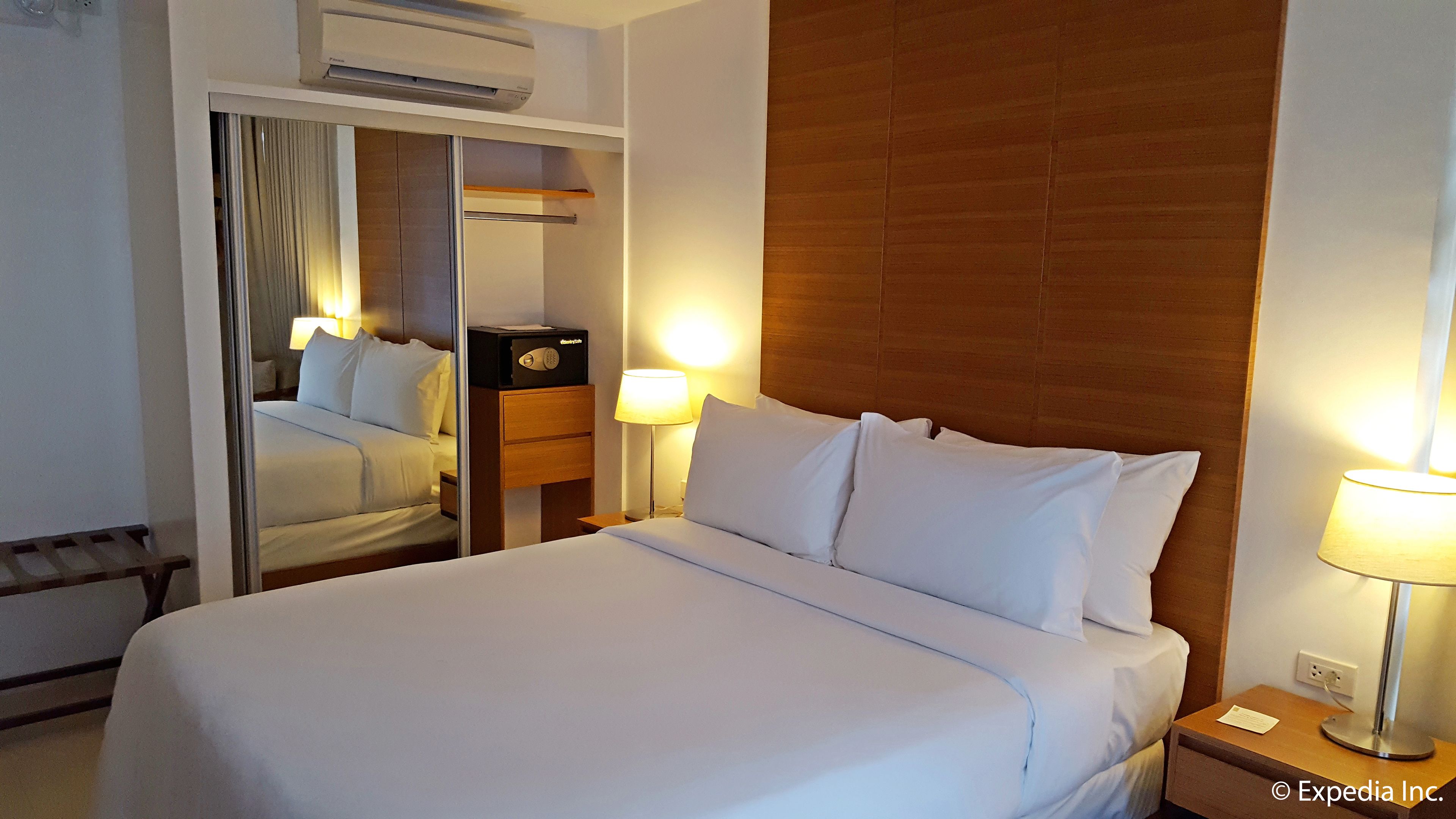 A hotel room with a large bed, a wooden headboard, a bedside table with a lamp, a nightstand, and a mirror.