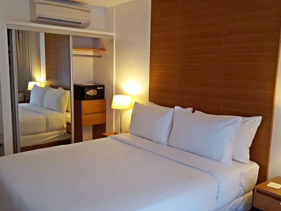 Een hotelkamer met een groot bed, een houten hoofdbord, een nachtkastje met een lamp, en een spiegel.