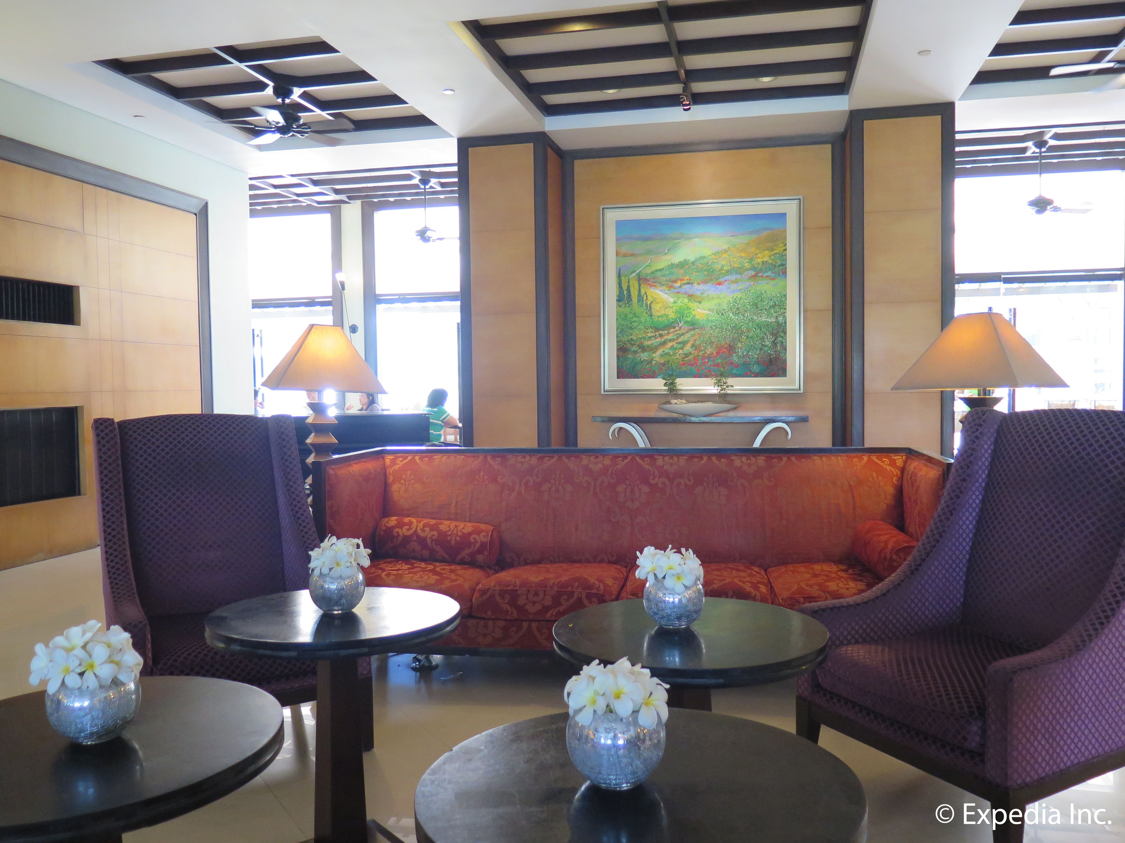 A lobby with a sofa, two armchairs, a table with a vase of flowers, a painting on the wall, and a piano.