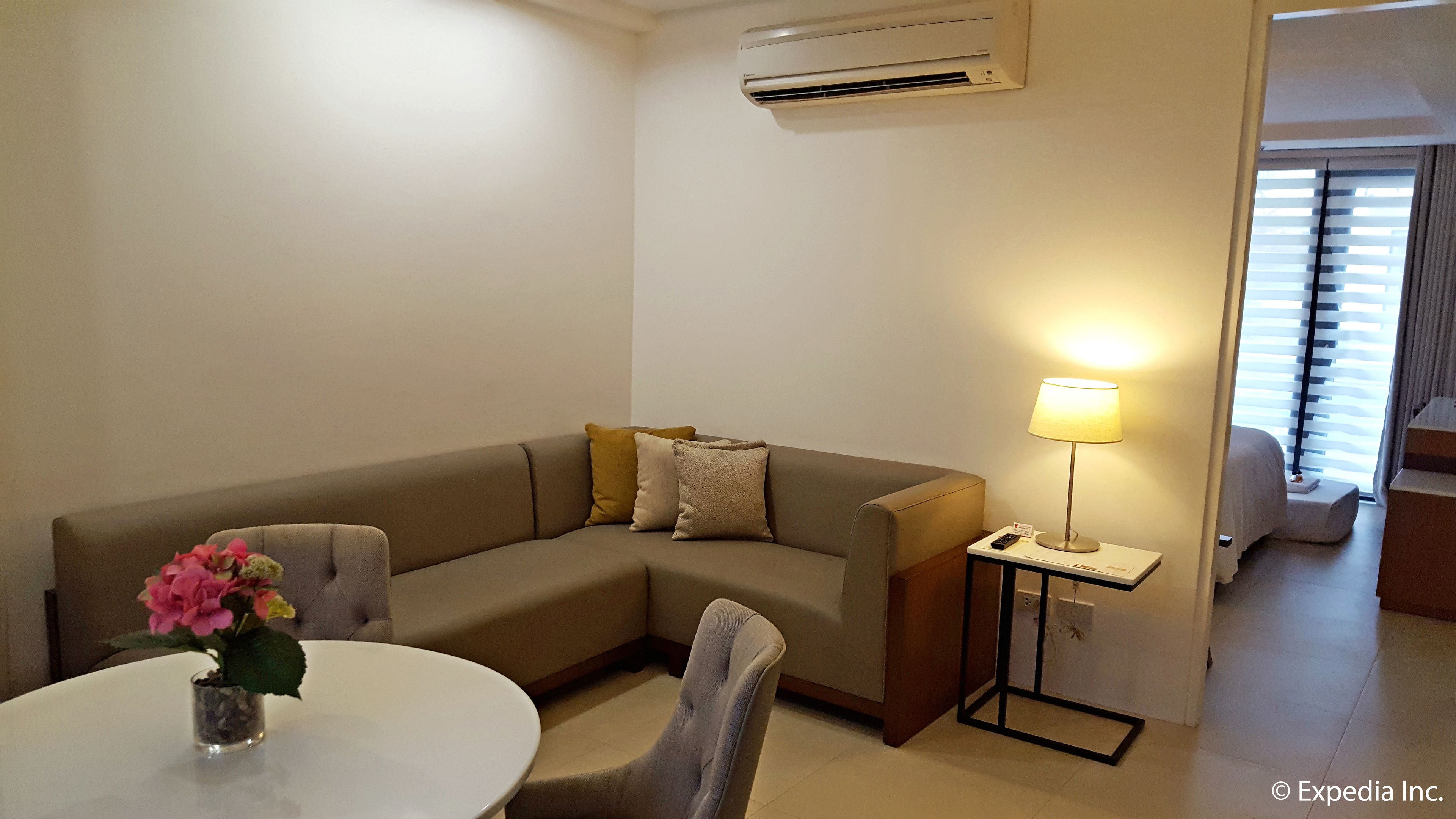 A modern living room with a sofa, a small table with a vase of flowers, a lamp, and an air conditioning unit on the wall.