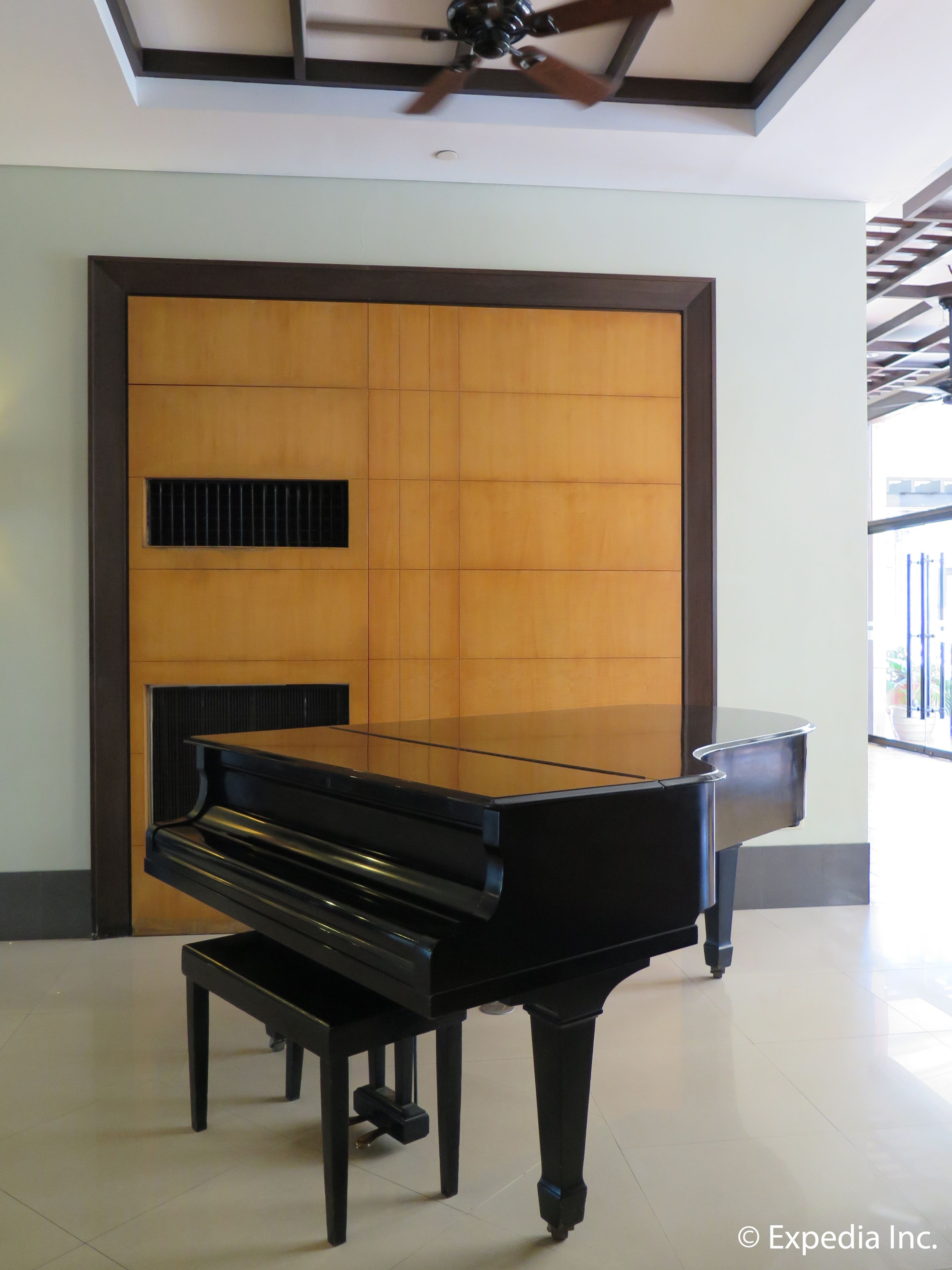 A grand piano in a spacious room with a wooden panel wall and a ceiling fan.