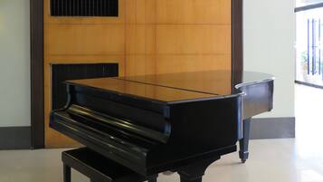 A grand piano in a spacious room with a wooden panel wall and a ceiling fan.