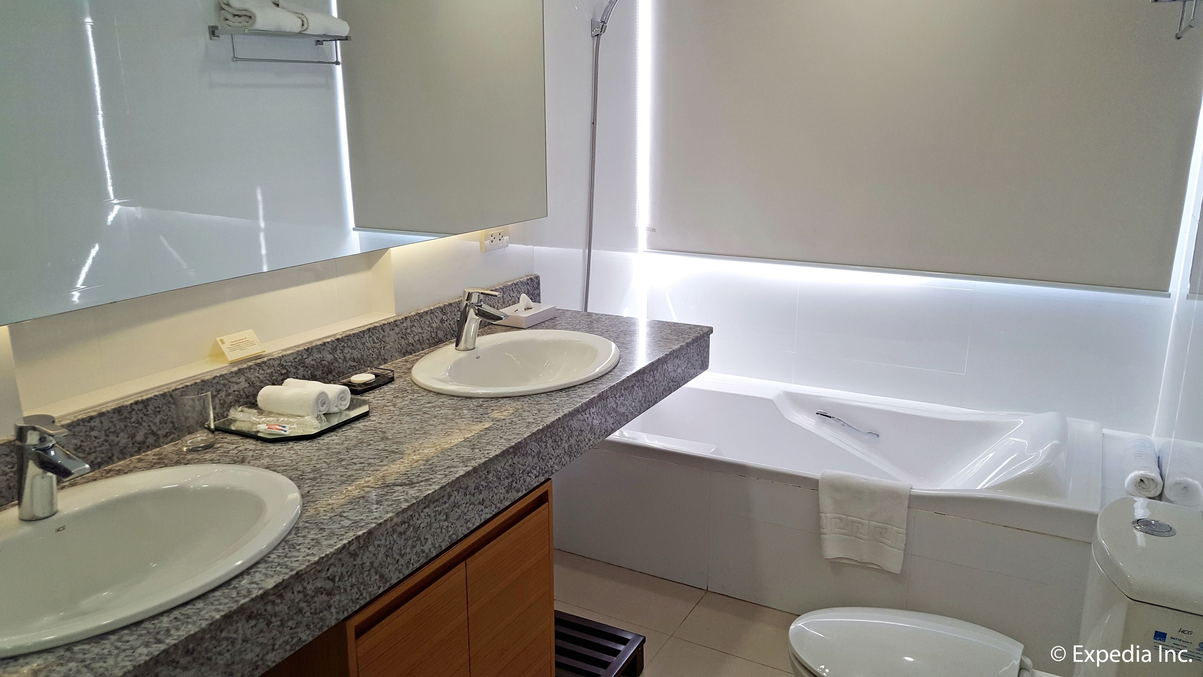 A modern bathroom with two sinks, a large mirror, and a bathtub.