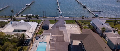 Vista aérea de una zona costera con un muelle largo que se adentra en el agua, una piscina y varios edificios de techos planos.