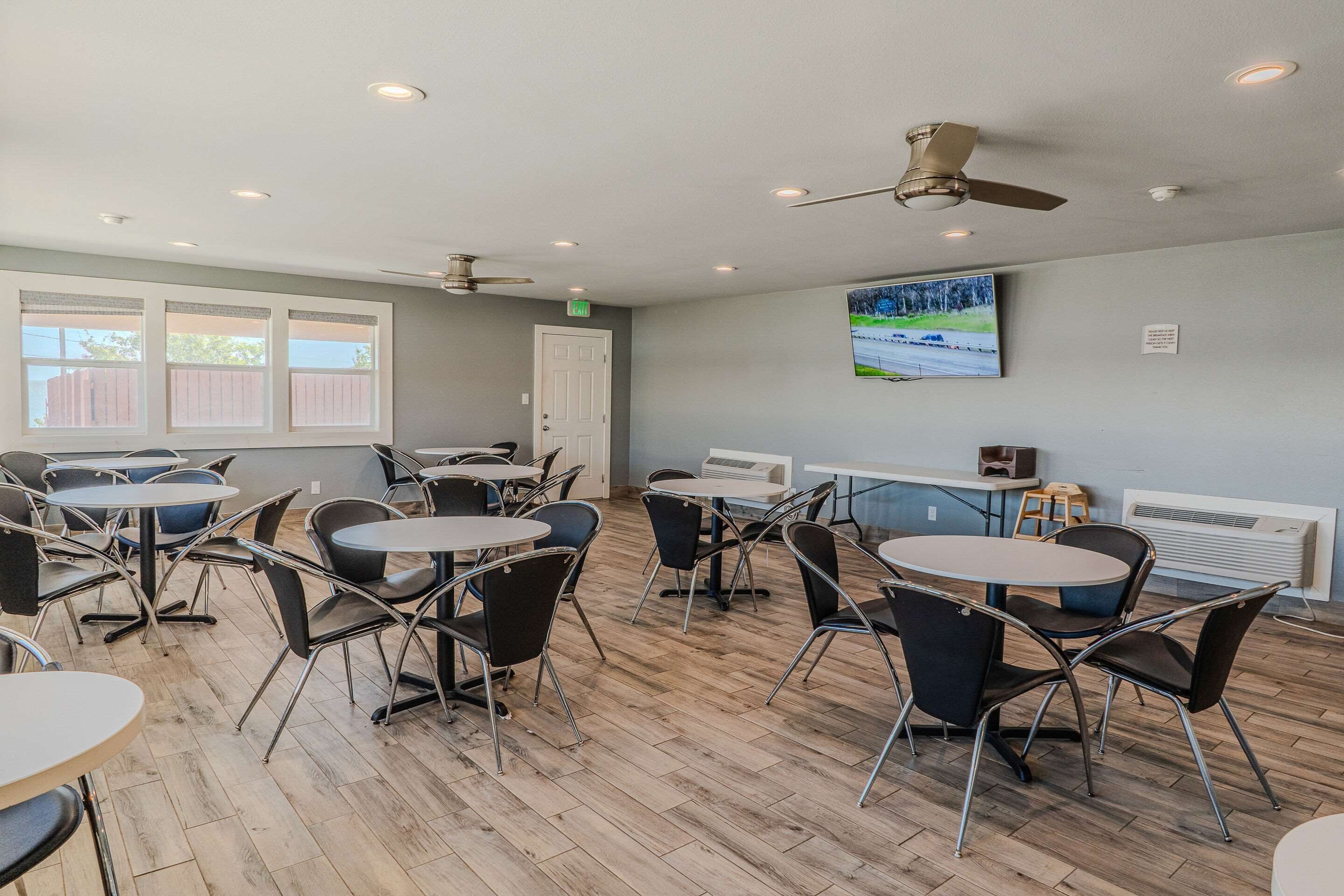Un espace repas avec des tables et des chaises rondes, des ventilateurs de plafond et une vue sur l’extérieur grâce à de grandes fenêtres.