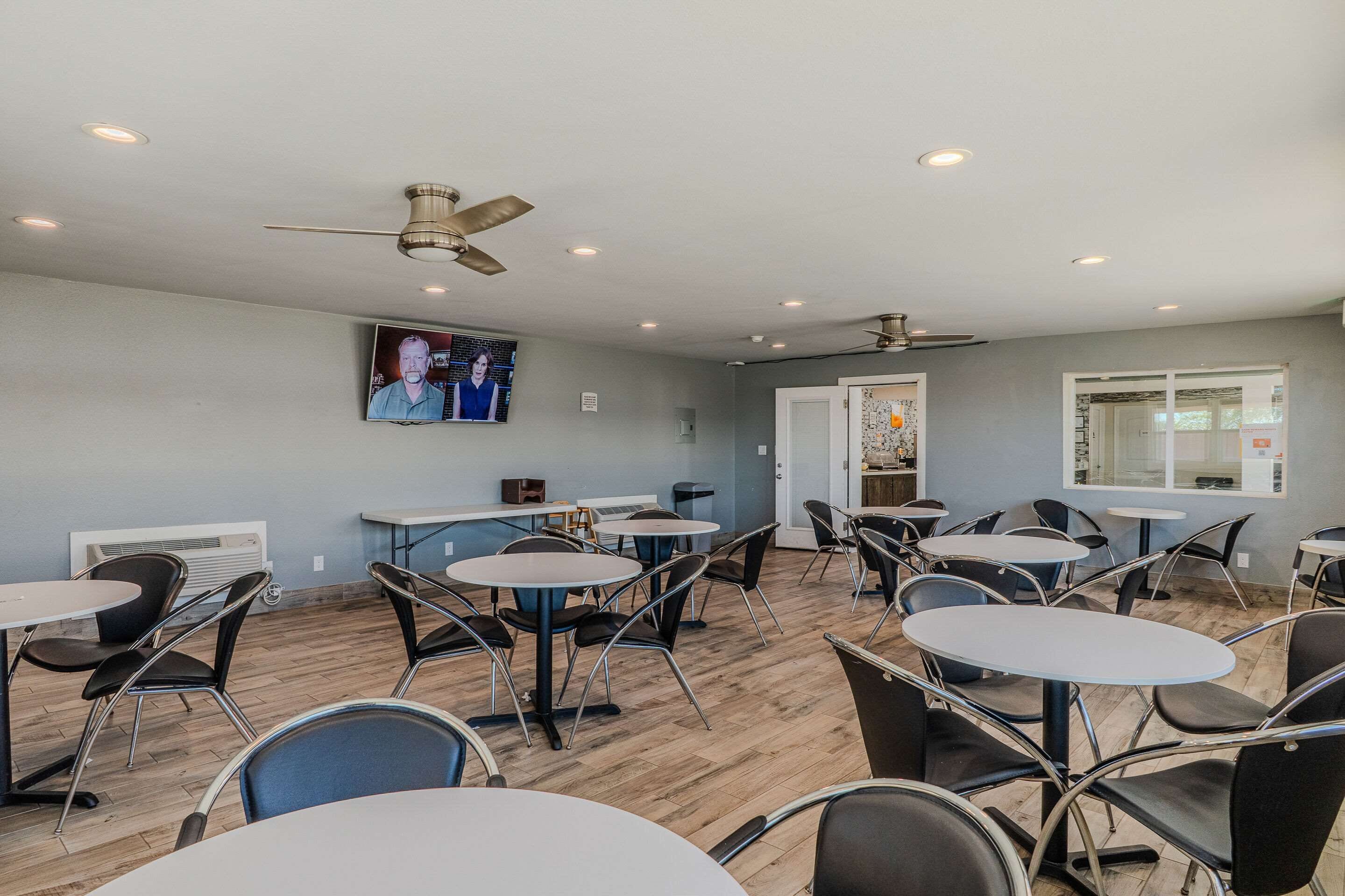 A conference room with round tables and chairs, a ceiling fan, recessed lighting, and a television screen on the wall.