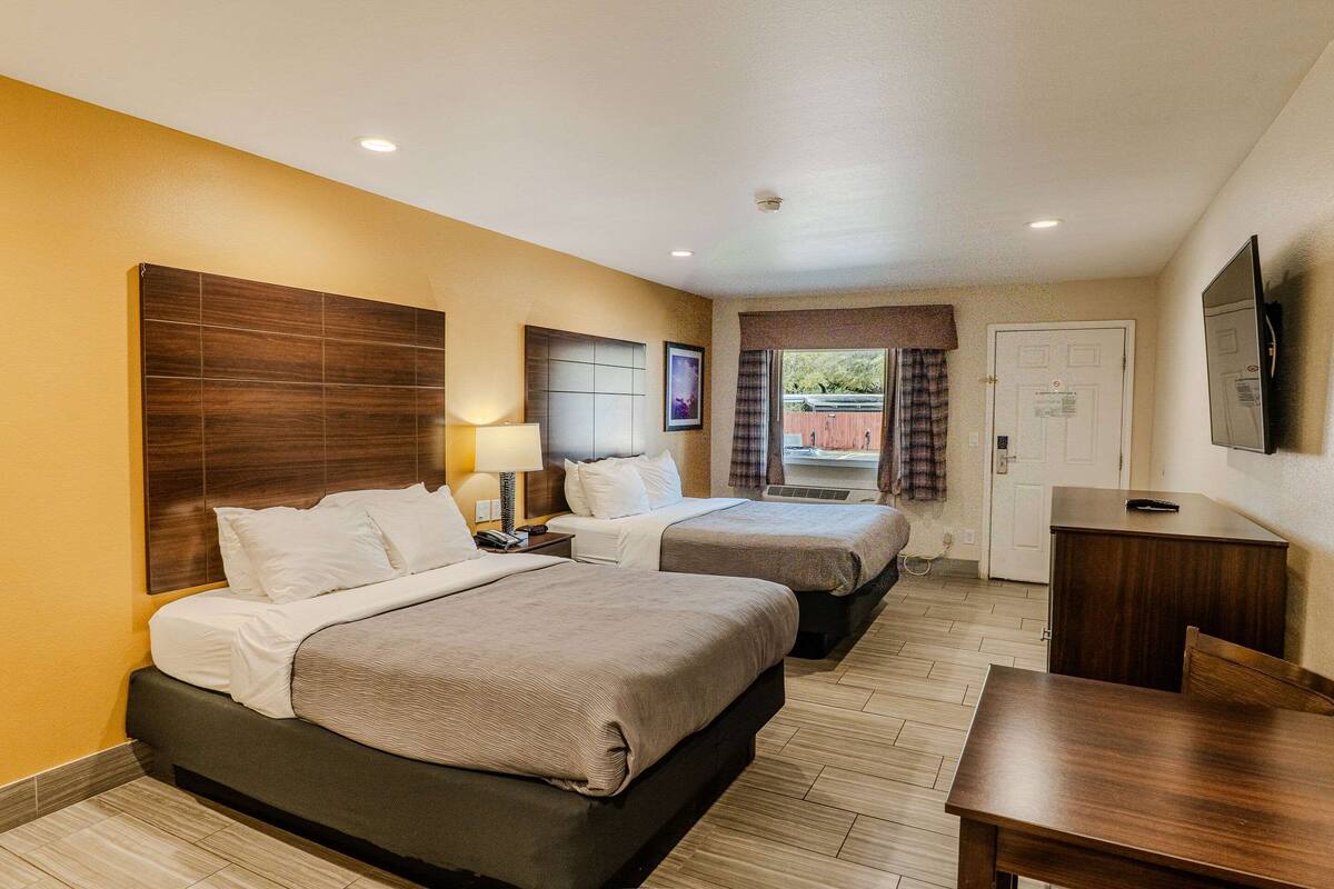 A hotel room with two beds, a desk, a TV, and a window with curtains.