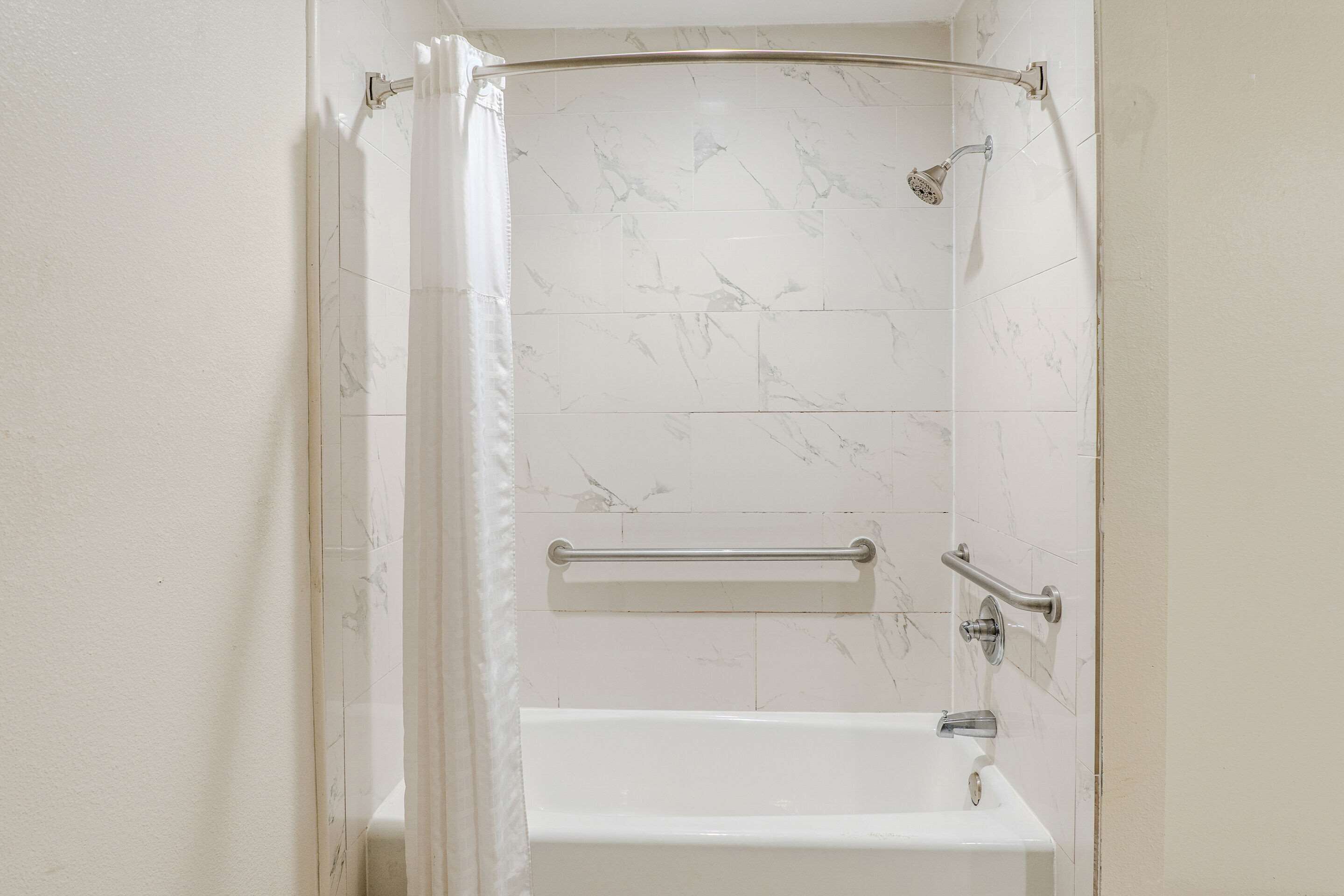 A bathroom with a shower, a grab bar, and a bathtub.