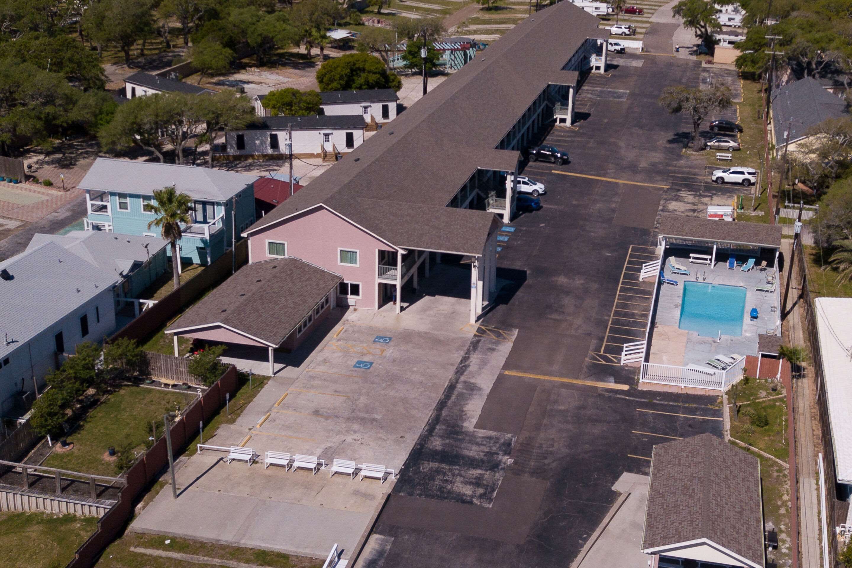 An aerial view of a parking lot with a swimming pool, a gas station, and several buildings.