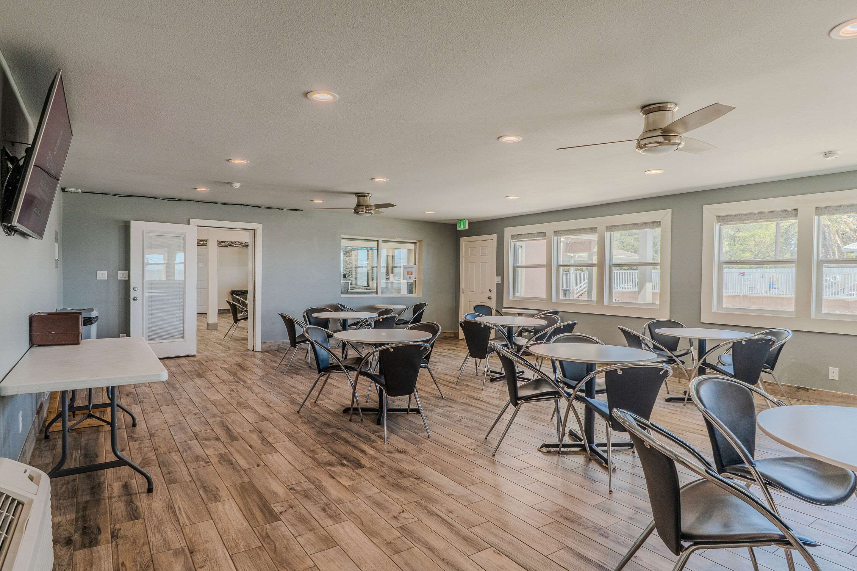 A spacious room with multiple tables and chairs, a ceiling fan, and large windows.