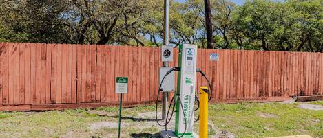 Una estación de carga pública para vehículos eléctricos con una valla de madera al fondo.