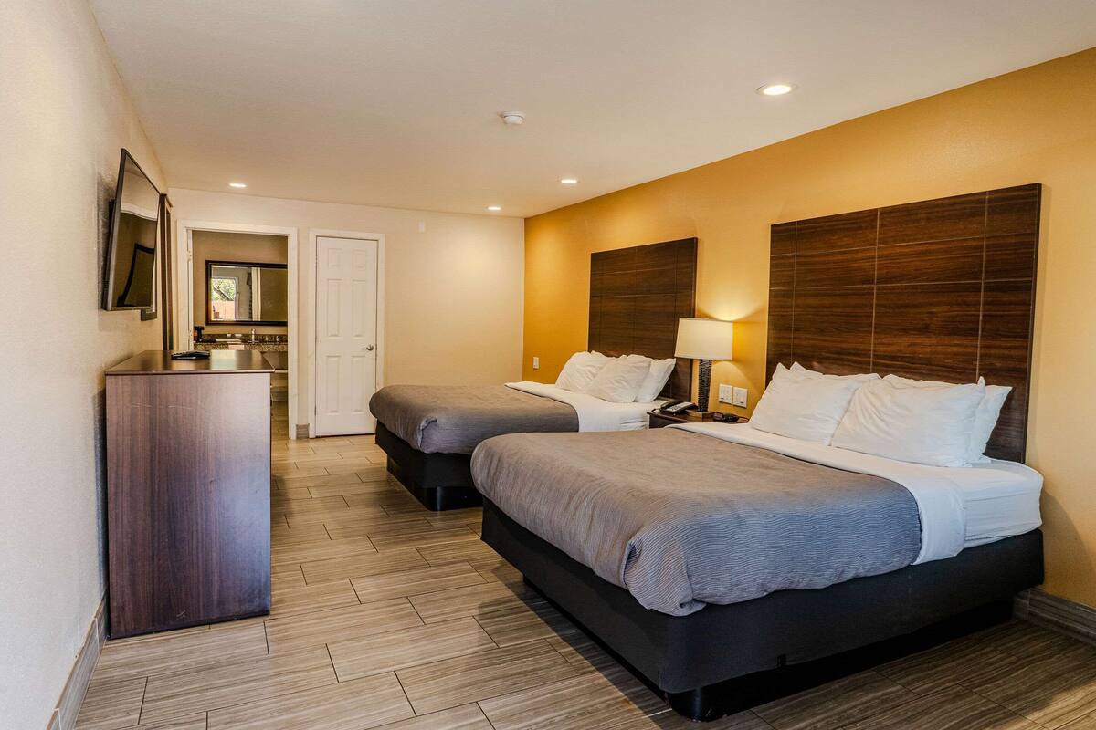 A hotel room with two beds, a desk, a mirror, and a door.