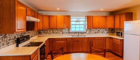 A kitchen with wooden cabinets, a white refrigerator, a stove, and a dining table with chairs.