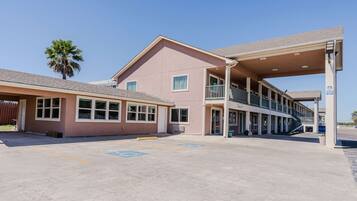 A building with a covered parking area, a staircase, and a palm tree.