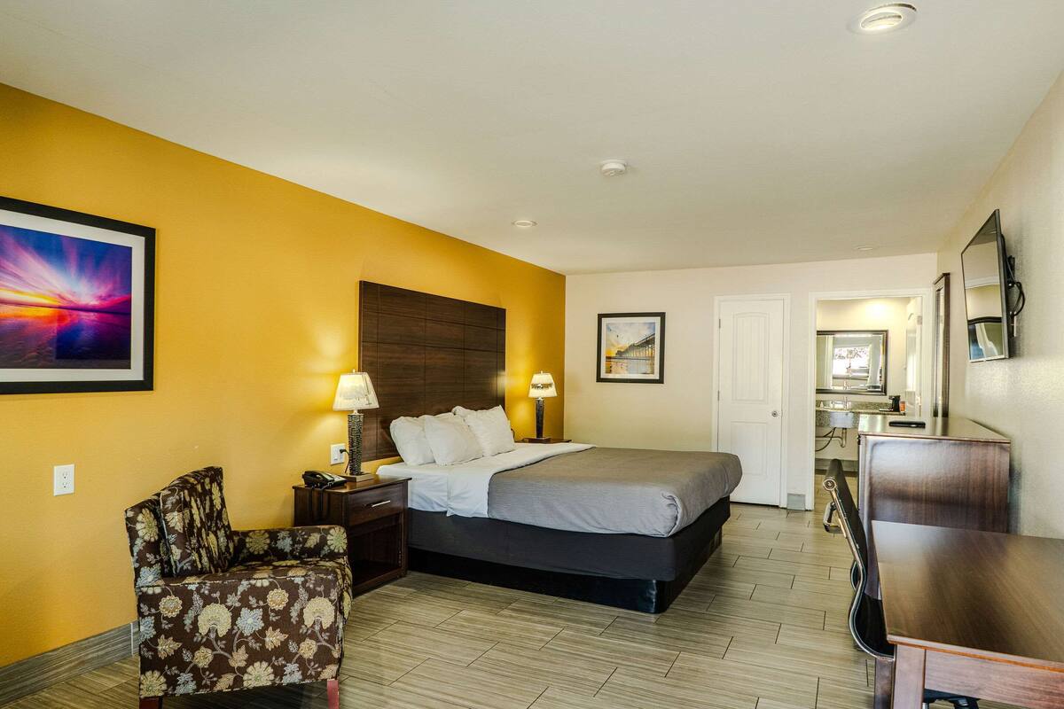A hotel room with a bed, a chair, a desk, and a bathroom visible through an open door.