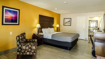 A hotel room with a bed, two bedside tables with lamps, a chair, a desk, and a bathroom visible through an open door.