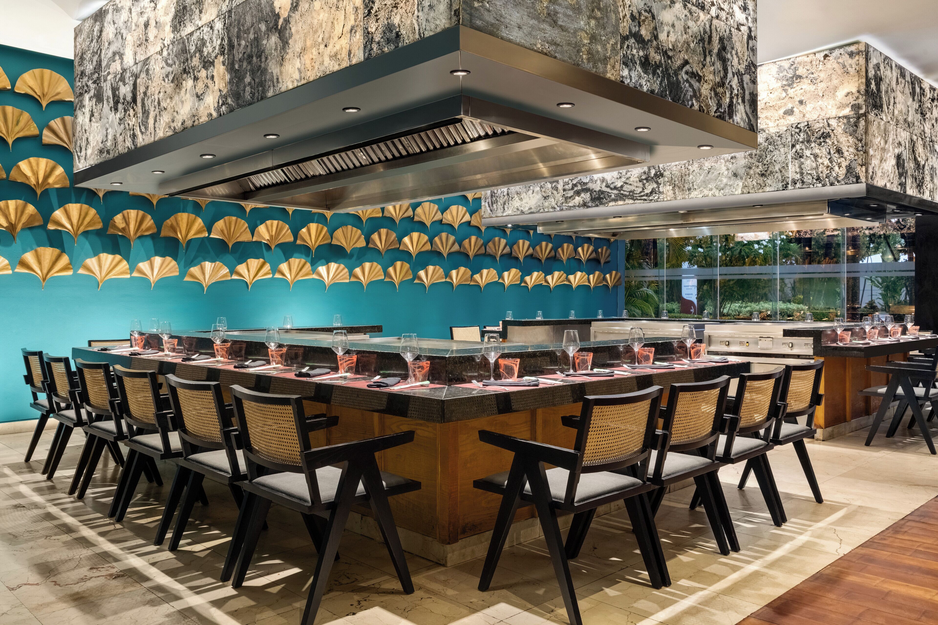 Un restaurante con una mesa larga compartida, sillas y una zona de cocina moderna.