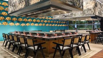 Un restaurante con una mesa larga compartida, sillas y una zona de cocina moderna.