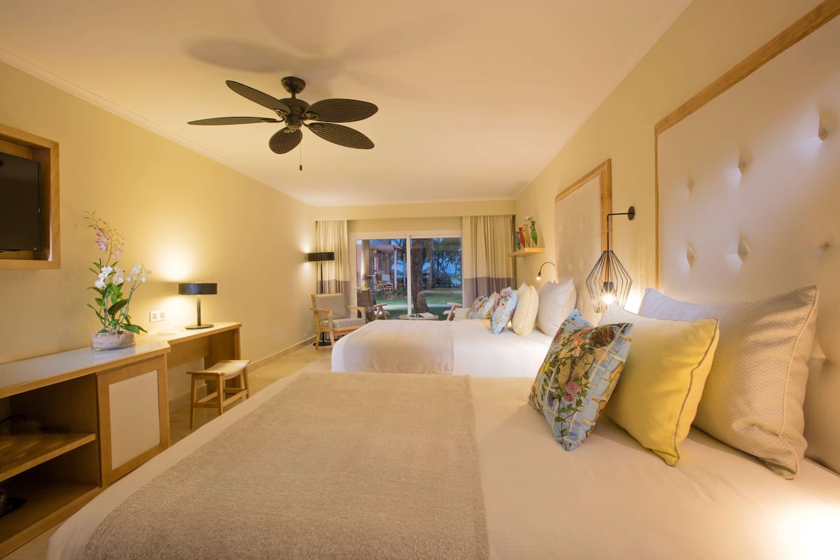 Een hotelkamer met twee bedden, een bureau, een stoel, een plafondventilator en uitzicht op de omgeving.