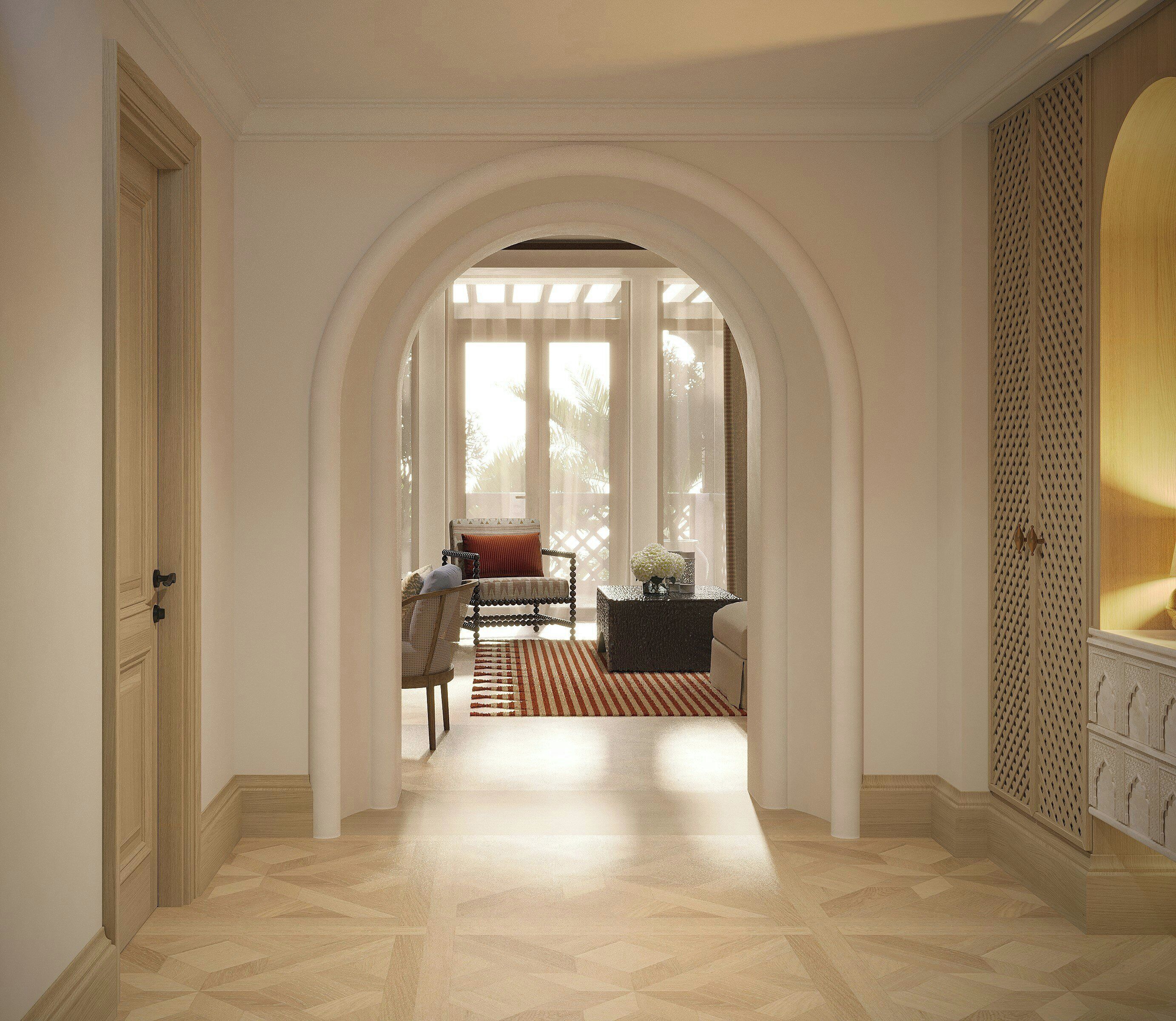A hallway with an arched doorway leading to a room with a bed, a chair, and a table.