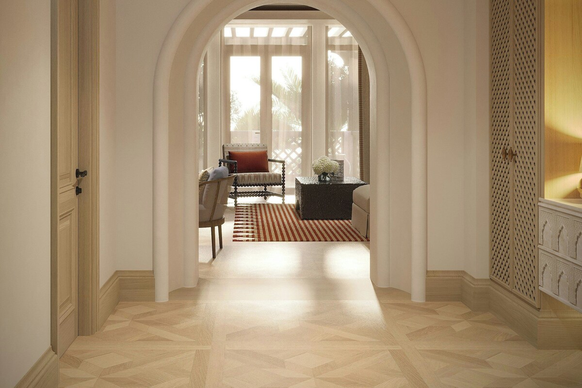 A hallway with an arched doorway leading to a room with a bed, a chair, and a table.