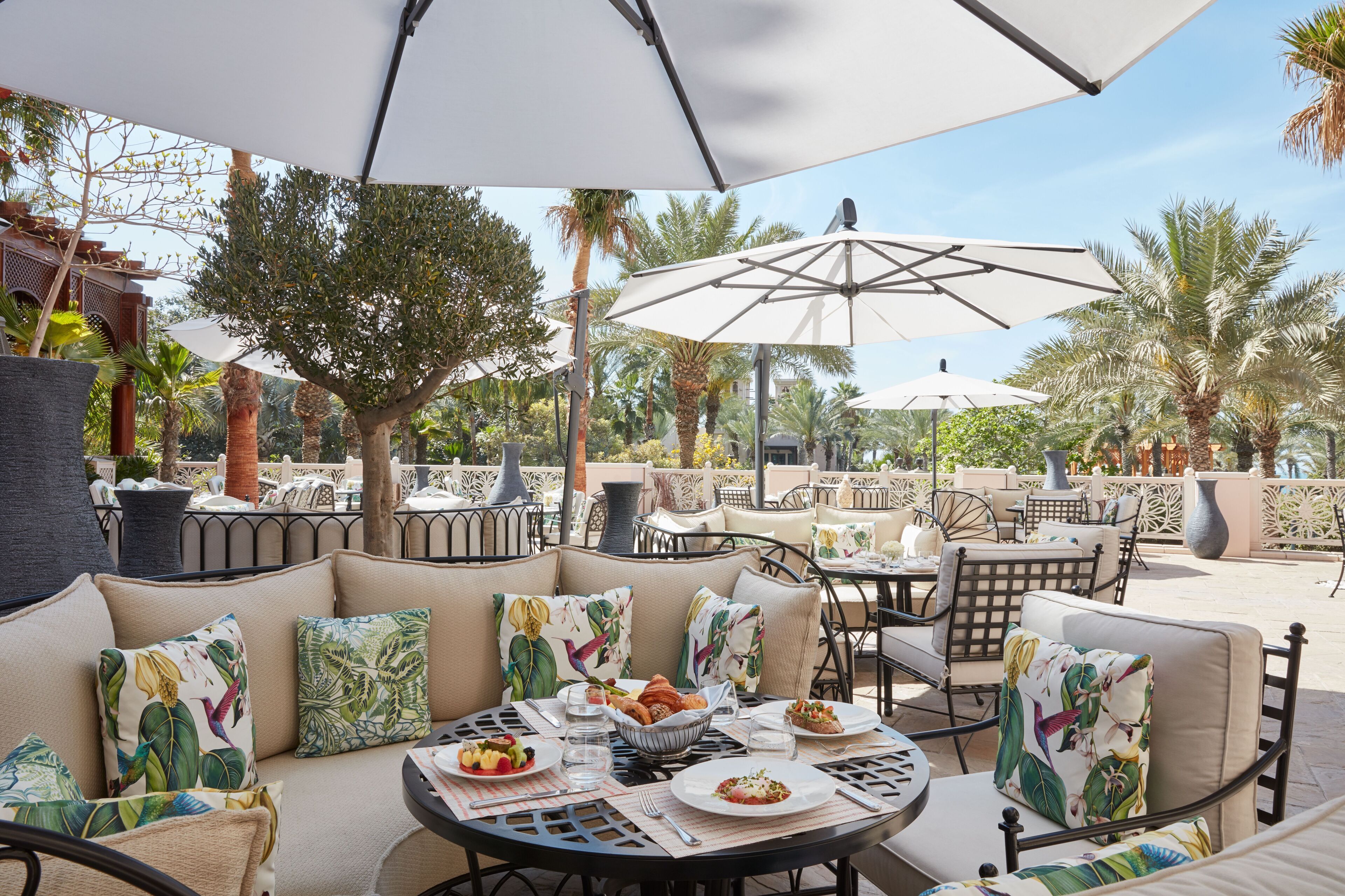 Un espace de restauration en plein air avec des tables rondes, des sièges rembourrés et des parasols pour faire de l’ombre.