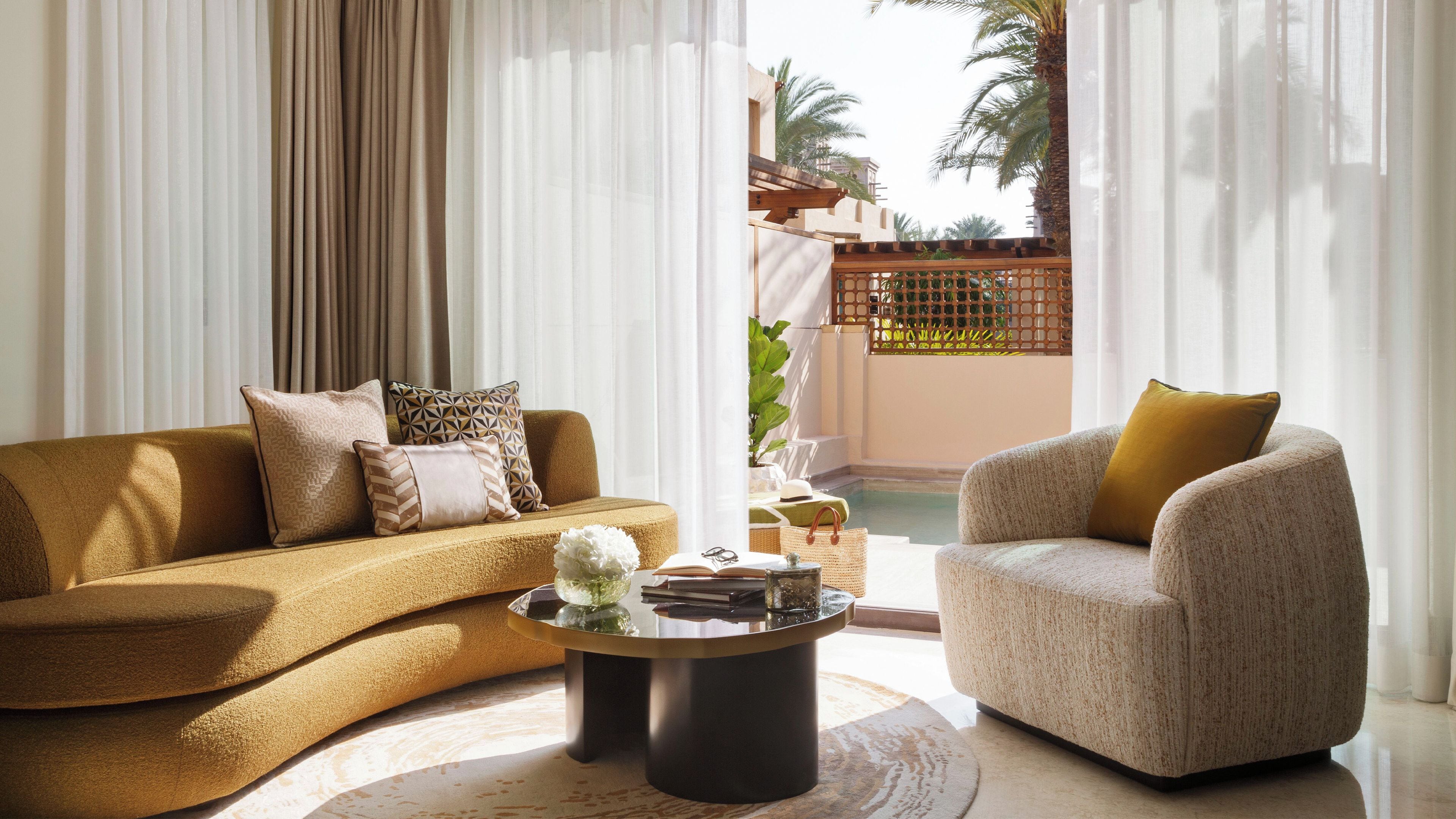 Ein Wohnzimmer mit einer Couch, Sesseln, einem Couchtisch und Blick auf ein Schwimmbad und Palmen.